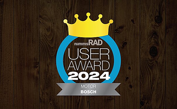 Icon with the text "nimms Rad User Award 2024": A golden crown above the text, enclosed by a blue circle. "MOTOR BOSCH" is written at the bottom. The background has a dark wood finish.
