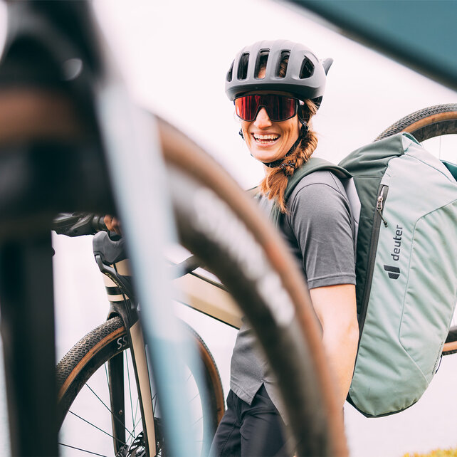 A woman wearing a helmet and sunglasses smiles as she carries her Gravel eBike on her shoulder.