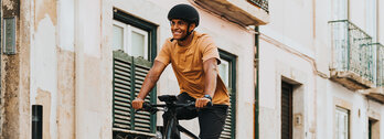 Mann mit Helm fährt auf einem eBike durch eine Gasse und lächelt dabei.
