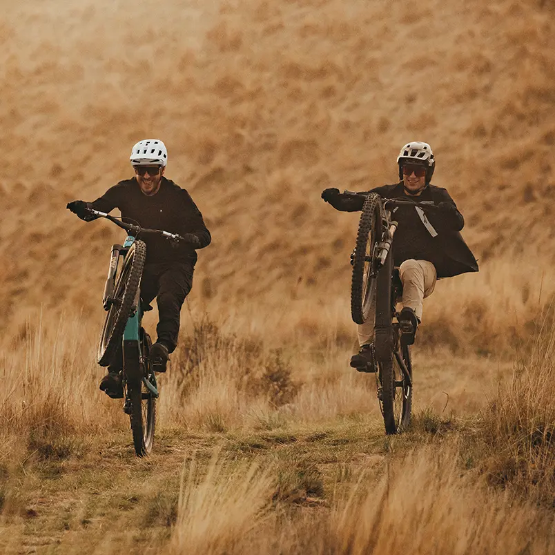 Zwei Personen fahren mit eMountainbikes über einen schmalen Trail in einer hügeligen Graslandschaft.