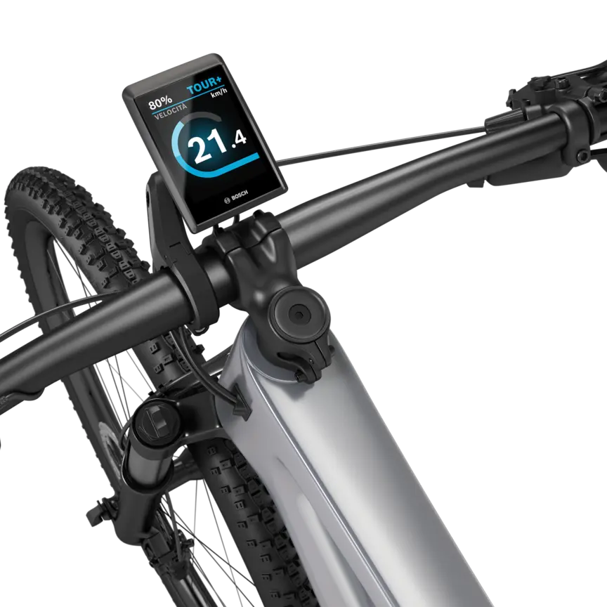 Una eMountainbike argentata con manubrio nero isolata su sfondo bianco. Un Kiox 500 è montato sul manubrio. Il display mostra la velocità in km/h, il livello di batteria e la modalità di guida.
