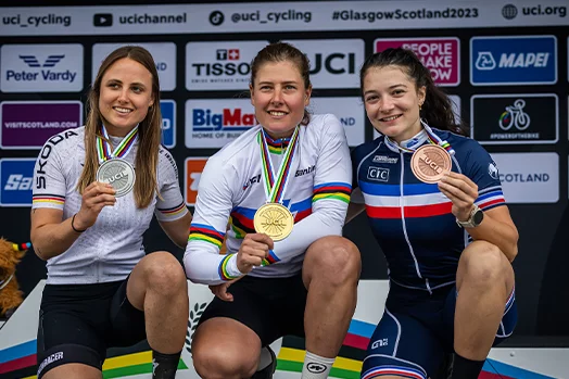 Three women pose squatting with bronze, silver, and gold medals.