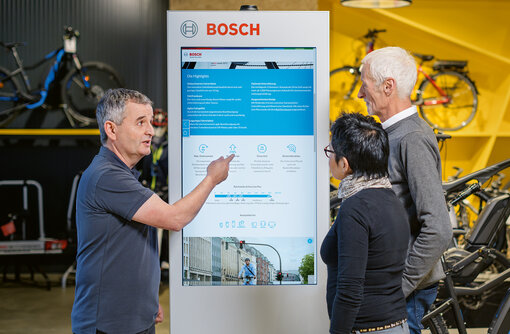 Ein eBike Fachhändler erläutert einem älteren Paar vor einer Infotafel die Bosch eBike Technik