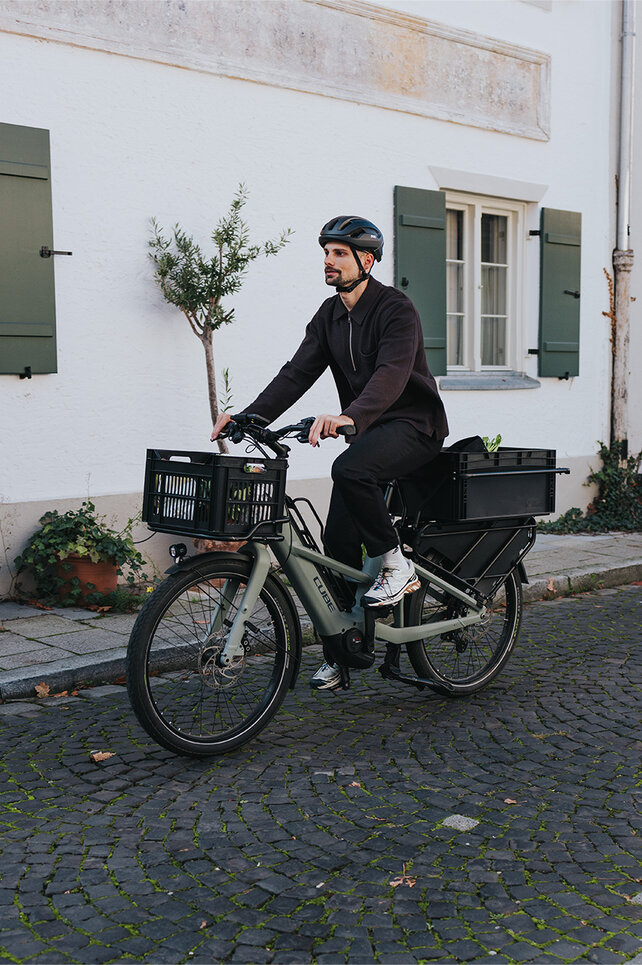Ein Mann fährt mit einem eCargo Bike durch einen Wohnort. 