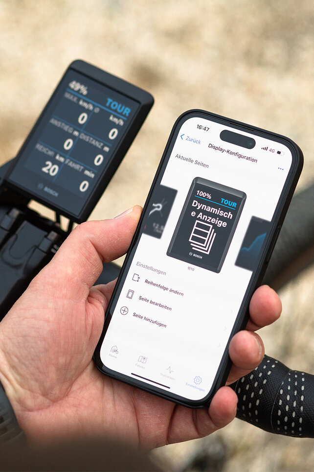Vor dem Lenker eines Gravelbikes wird ein Smartphone gehalten. Auf dem Display ist die Konfigurationsmöglichkeit der dynamischen Anzeige zu sehen.