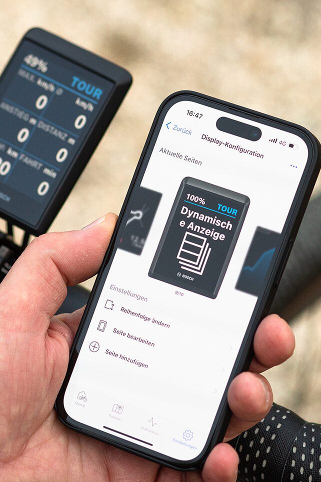 Vor dem Lenker eines Gravelbikes wird ein Smartphone gehalten. Auf dem Display ist die Konfigurationsmöglichkeit der dynamischen Anzeige zu sehen.