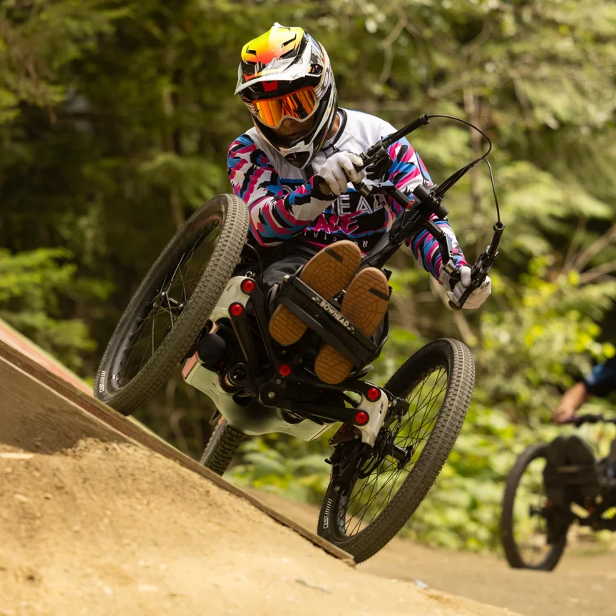 Tarek Rasouli, wearing a helmet and protective gear, rides his handbike over a wooden structure in a bike park.