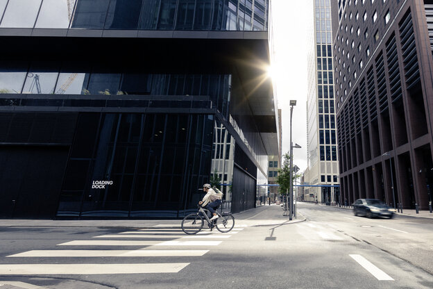 Un homme se promène à vélo électrique dans les rues de Francfort-sur-le-Main, en passant devant des bâtiments modernes et une architecture urbaine.