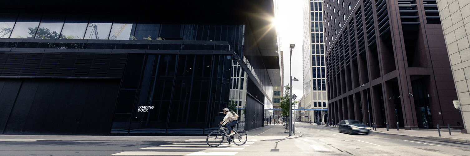 A man rides his eBike through the streets of Frankfurt am Main, passing by modern buildings and urban architecture.