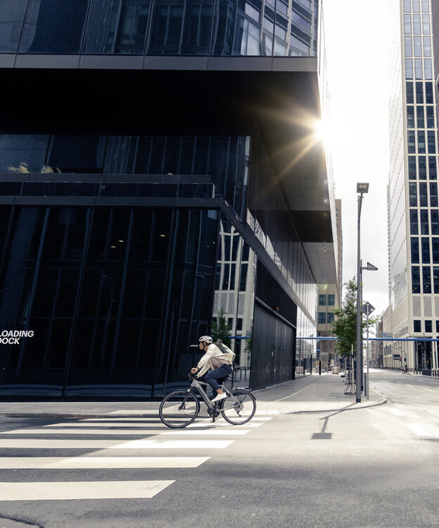 Un homme se promène à vélo électrique dans les rues de Francfort-sur-le-Main, en passant devant des bâtiments modernes et une architecture urbaine.