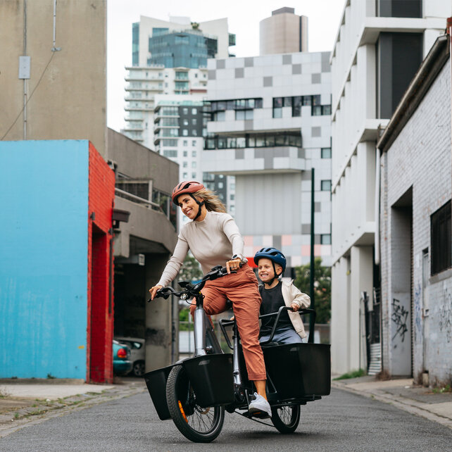 eBikerin fährt mit ihrem Kind auf einem eCargo Bike um eine Kurve.