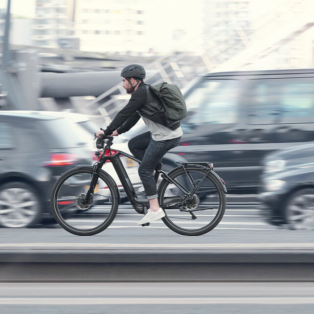 Un VAE utilisateur roule le long d'une route à côté de voitures, tout sauf lui est légèrement flou.