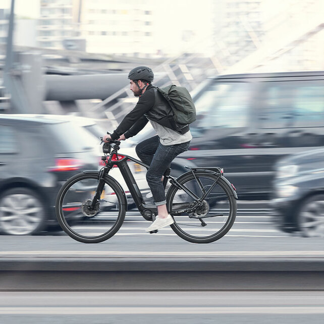 Kierowca eBike jedzie wzdłuż ulicy obok samochodów, wszystko oprócz niego jest lekko rozmazane.