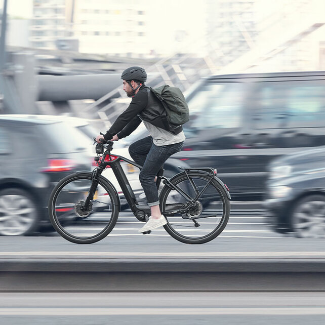 En eBike-cyklist cyklar längs en gata bredvid bilar, allt utom honom är lätt suddigt.