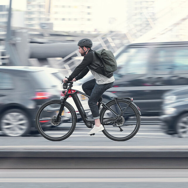 An eBike rider drives down a road next to Autoslong, everything except him is slightly blurry.