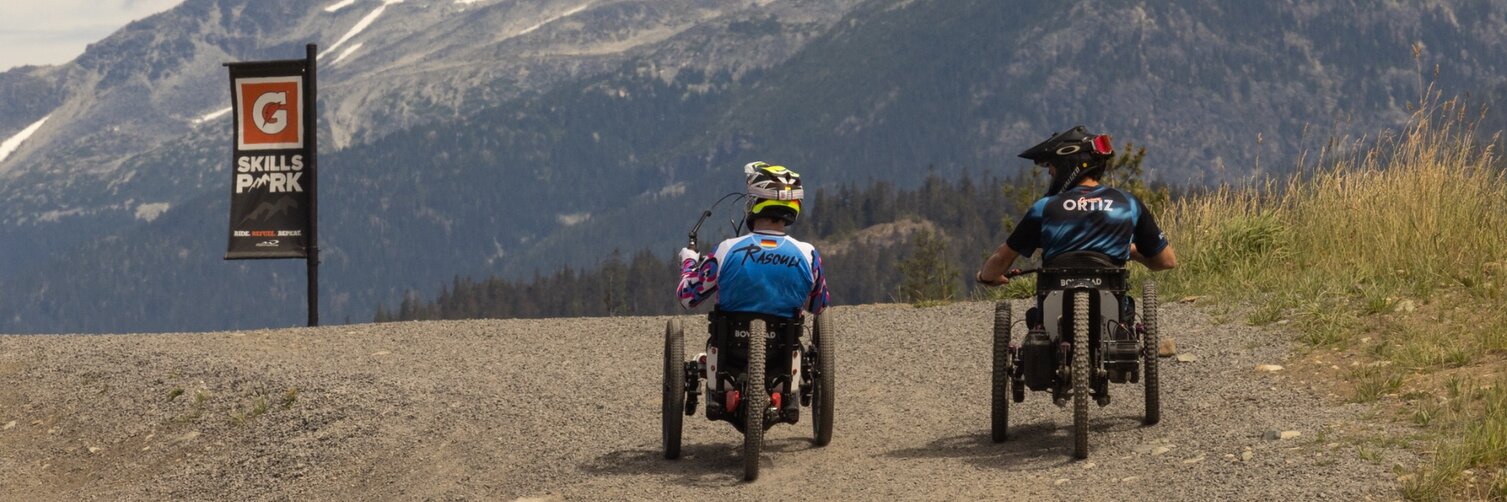 Tarek Rasouli rides his handbike alongside another mountain biker on a mountain trail. 