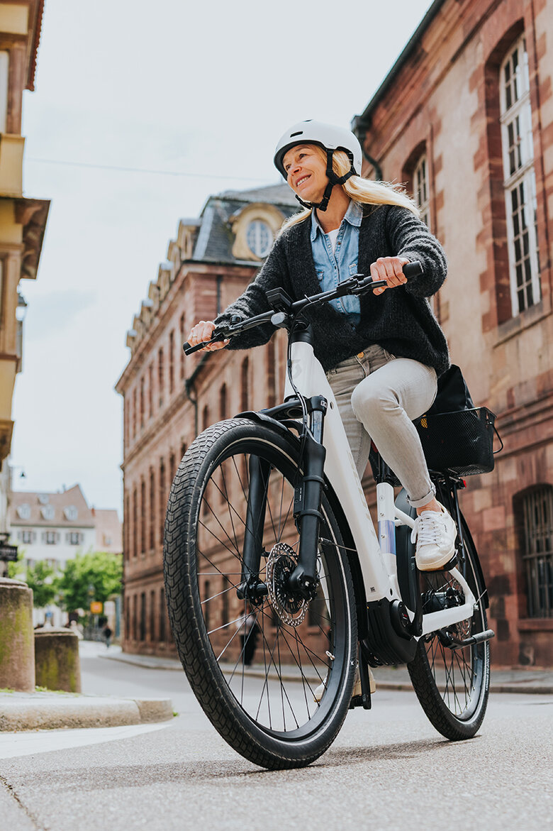 Eine lächelnde Frau biegt mit ihrem weißen eBike rechts ab.