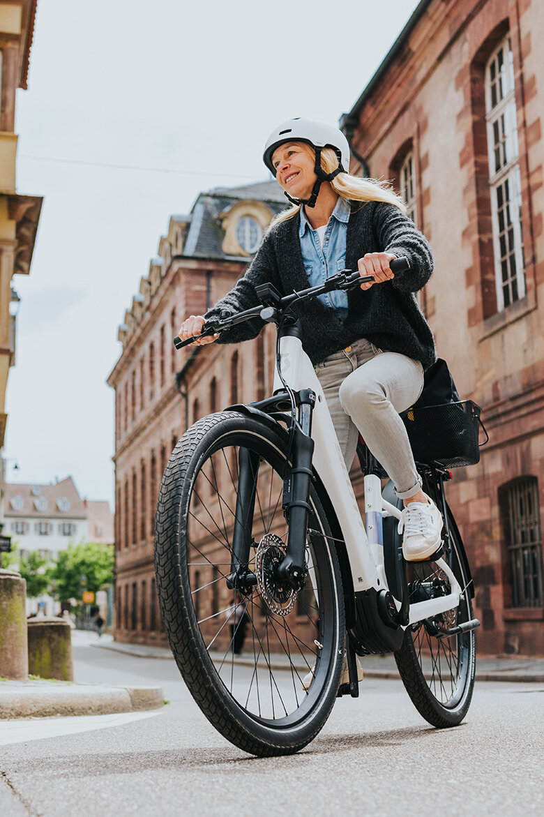 Eine lächelnde Frau biegt mit ihrem weißen eBike rechts ab.
