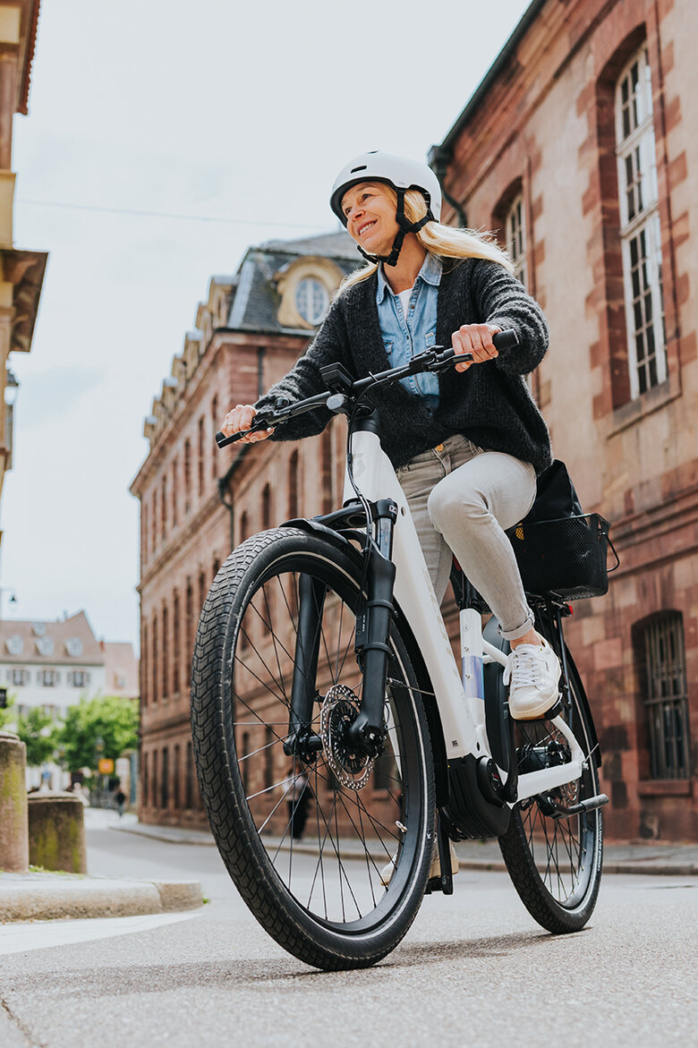 Eine lächelnde Frau biegt mit ihrem weißen eBike rechts ab.