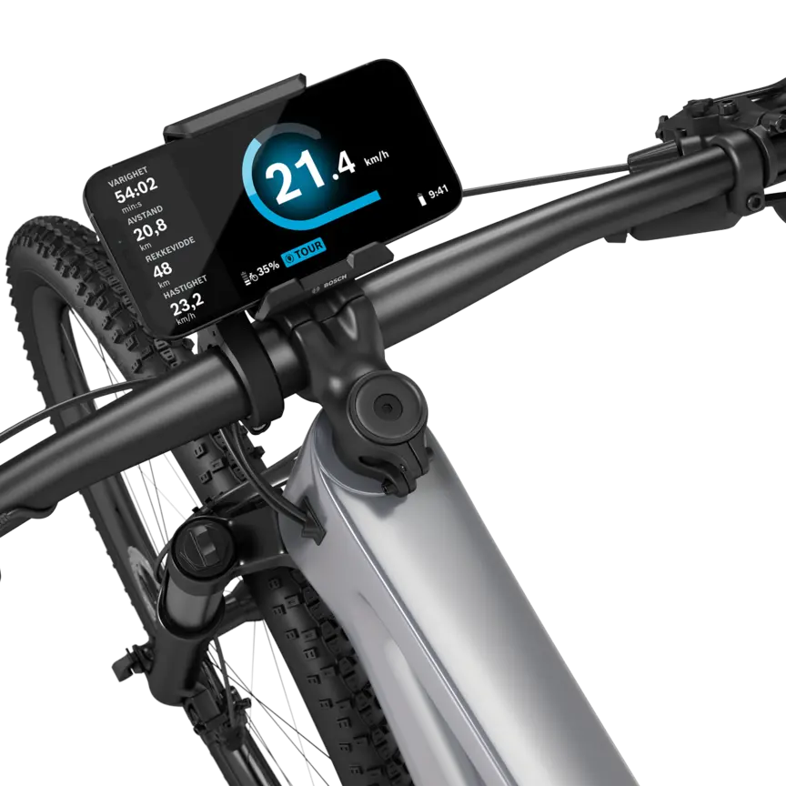 En sølvfarget elektrisk terrengsykkel med sort styre, isolert mot hvit bakgrunn. En SmartphoneGrip er montert på styret, og en smarttelefon er festet i den. Den åpne eBike Flow App viser fart i km/t, varighet i minutter, tilbakelagt distanse i kilometer, rekkevidde i kilometer og gjennomsnittshastighet. I tillegg vises batteristatus og kjøremodus.