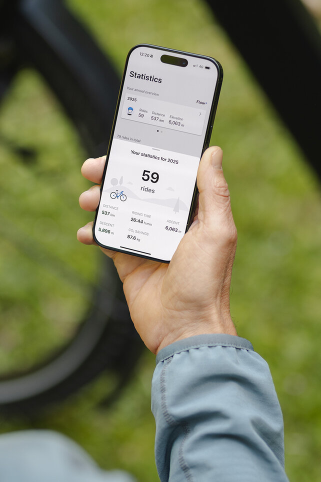 A person holds a smartphone and checks the statistics in the eBike Flow app.