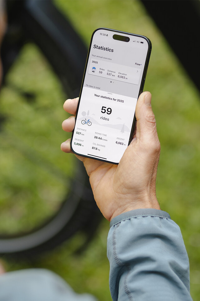 Osoba drží v ruce chytrý telefon a sleduje statistiky v aplikace eBike Flow.