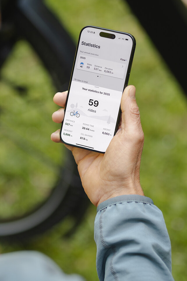 Osoba drží v ruce chytrý telefon a sleduje statistiky v aplikace eBike Flow.