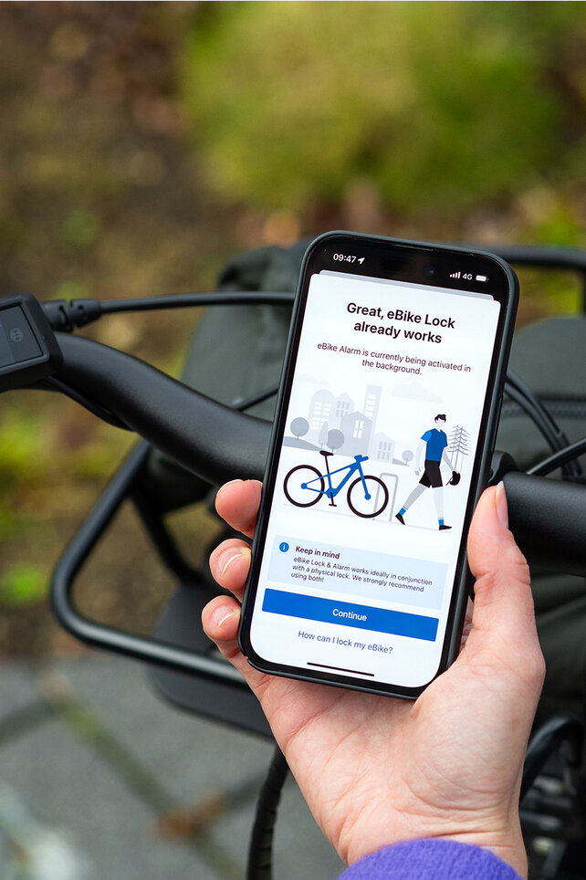 Blick über die Schulter einer Person, die ein Smartphone hält und in der eBike Flow App die Funktionen eBike Lock und eBike Alarm aktiviert.