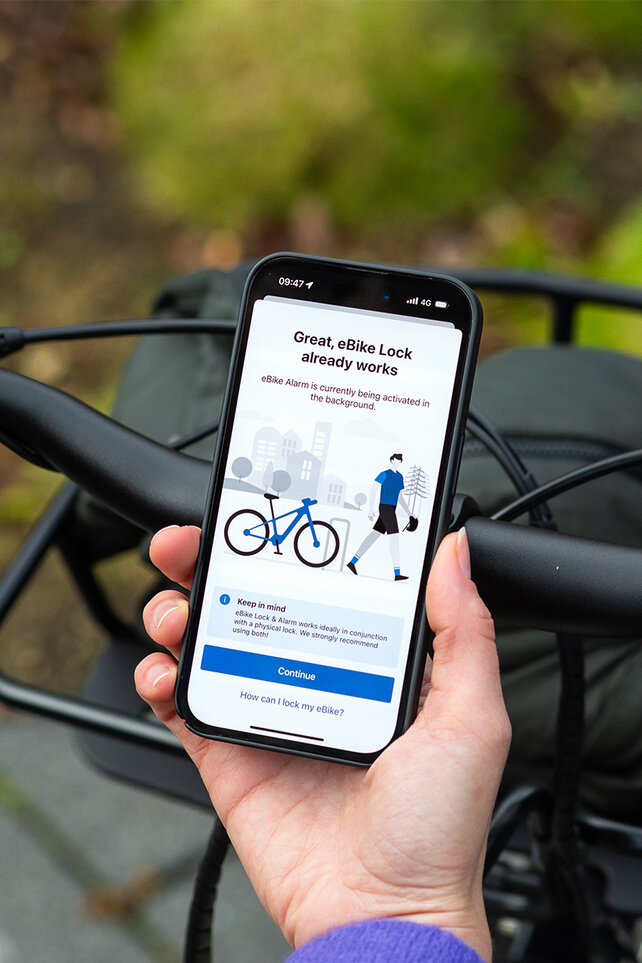 Se over skulderen til en person som holder en smarttelefon og aktiverer eBike Lock- og eBike Alarm-funksjonene i eBike Flow-app.