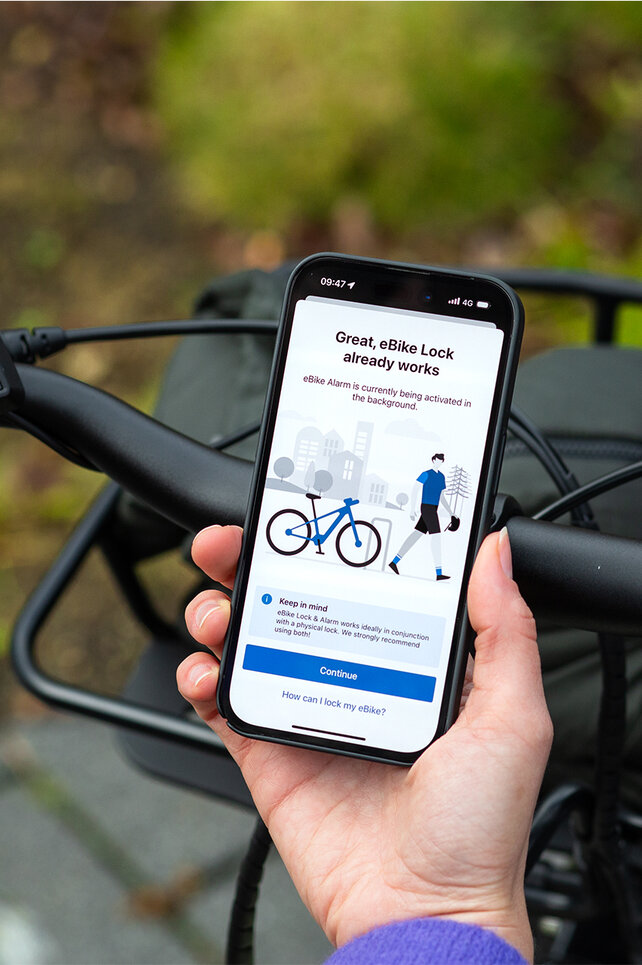Looking over the shoulder of a person holding a smartphone and activating the eBike Lock and eBike Alarm functions in the eBike Flow app.