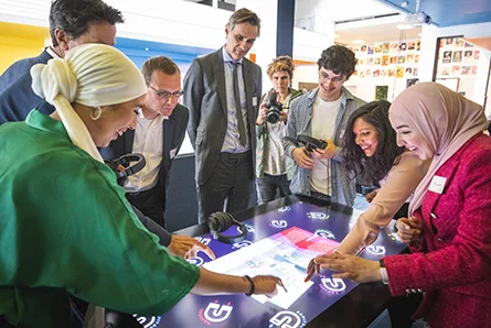 Een groep mensen staat rondom een groot display en gebruikt het interactief.