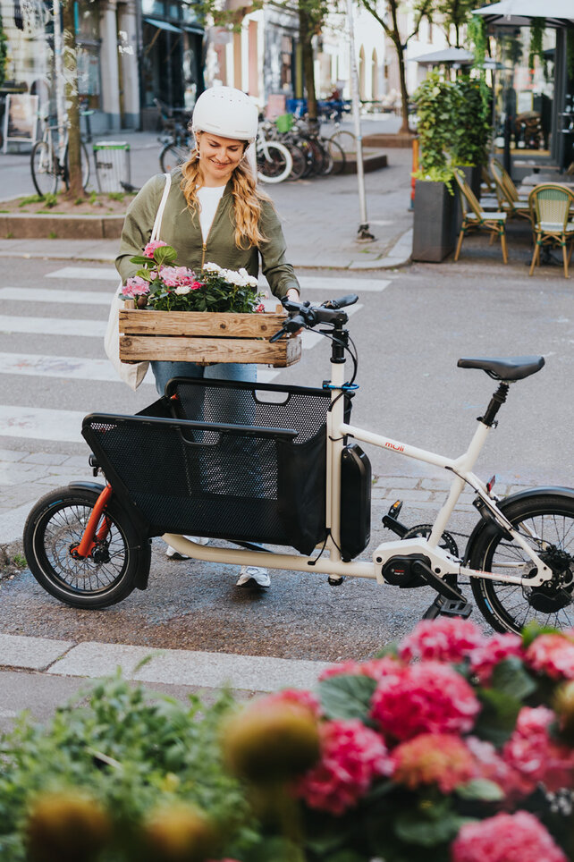 Femme souriante portant un panier de fleurs vers son VAE Cargo.