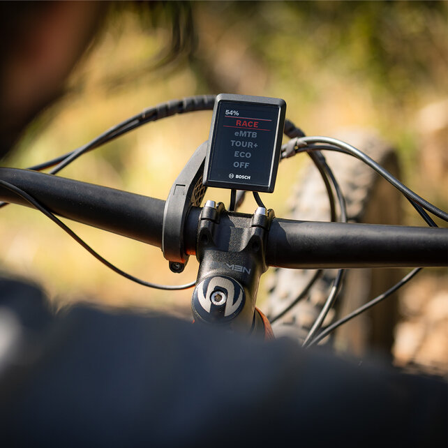 Guardando oltre la spalla di un eBiker sul suo display, dove è selezionata la modalità Race.