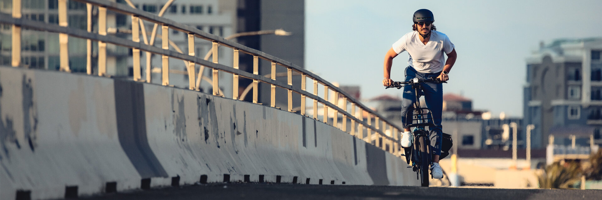 An eBiker rides over a bridge in the background of a city.