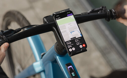 Nahaufnahme eines SmartphoneGrip Verticals, das an einem Lenker befestigt ist. Das Smartphone befindet sich im Navigationsmodus und zeigt eine Routenführung an.