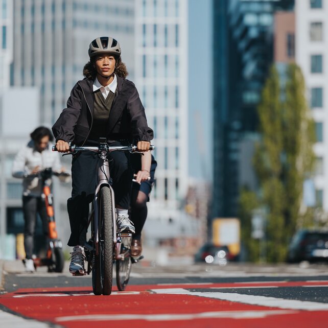 Eine Frau fährt mit dem eBike auf einem roten Radweg in der Stadt.