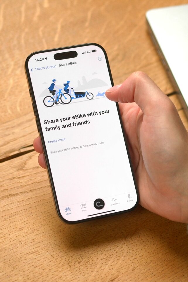 Une personne est assise à la table et a ouvert l'application eBike Flow sur son smartphone pour partager son VAE avec quelqu’un.