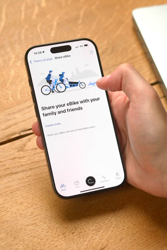 Une personne est assise à la table et a ouvert l'application eBike Flow sur son smartphone pour partager son VAE avec quelqu’un.