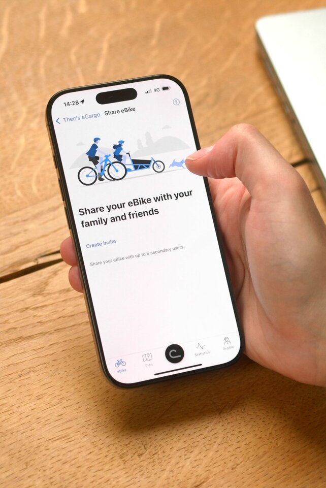 En person sidder ved bordet og har åbnet eBike Flow-app på sin smartphone for at dele sin eBike med en anden.
