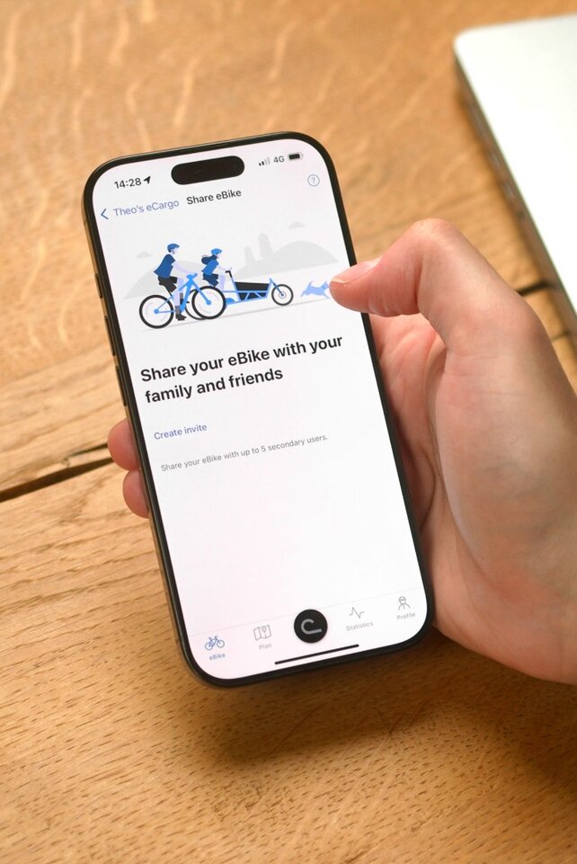 En person sitter ved bordet og har åpnet eBike Flow-app på smarttelefonen sin for å dele elsykkel med noen.
