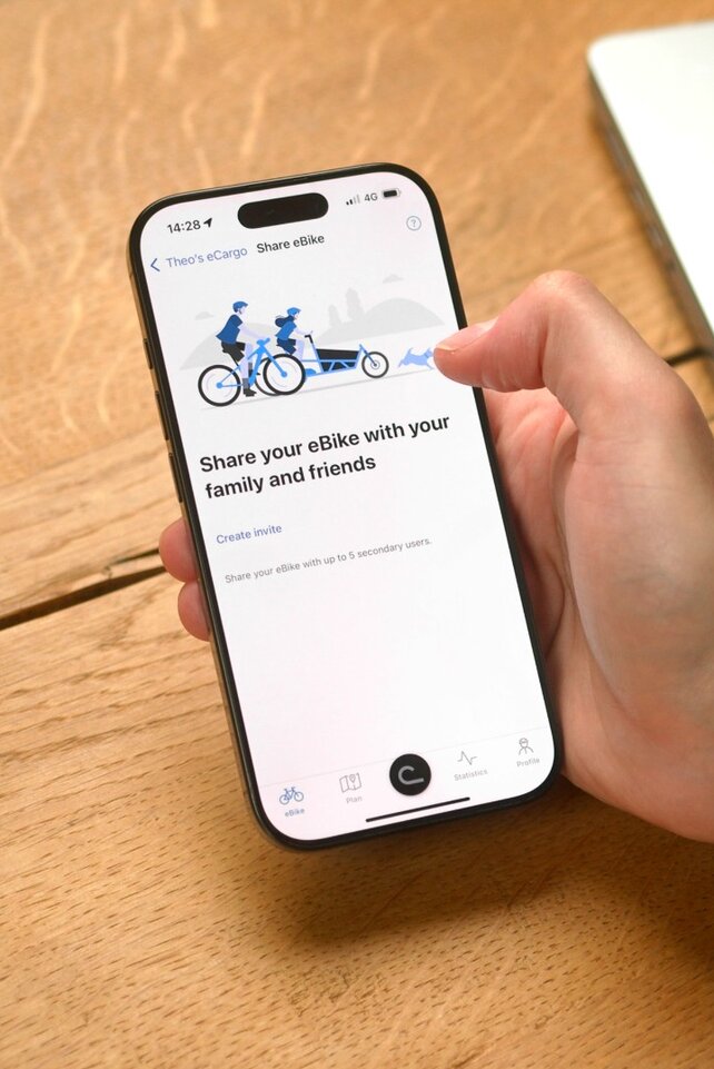 A person is sitting at the table with the eBike Flow app open on their smartphone, ready to share their eBike with someone.