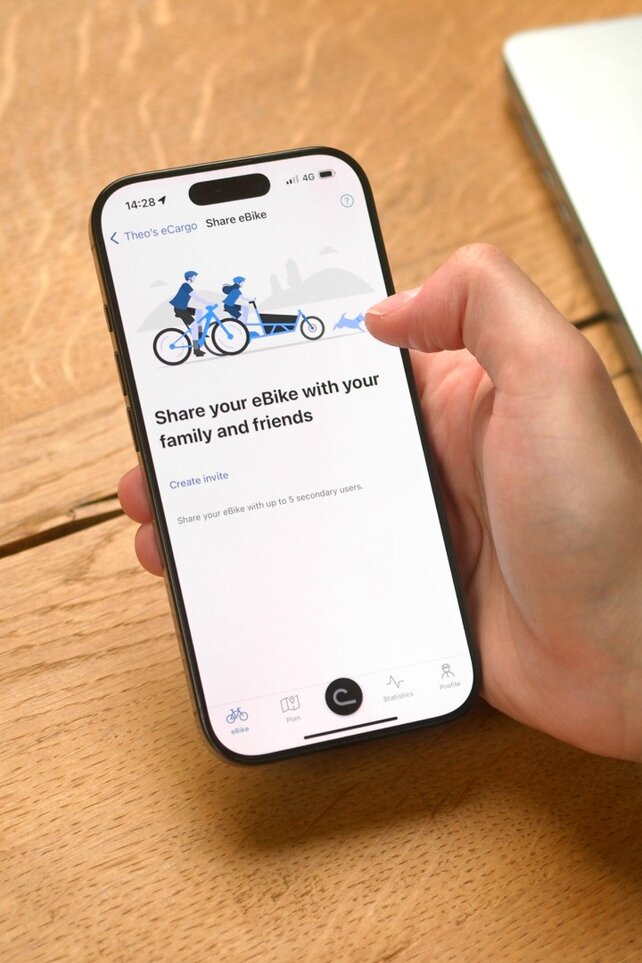 Osoba siedzi przy stole i otworzyła aplikacja eBike Flow na swoim smartfonie, aby udostępnić komuś swój rower ze wspomaganiem elektrycznym / e-rower.