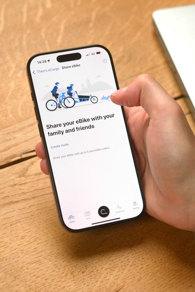 A person is sitting at the table with the eBike Flow app open on their smartphone, ready to share their eBike with someone.