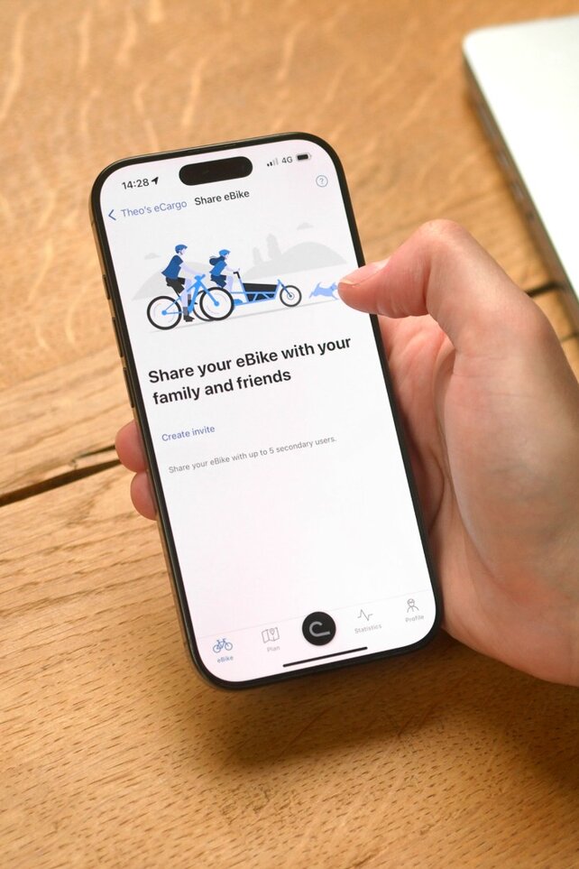 A person is sitting at the table with the eBike Flow app open on their smartphone, ready to share their eBike with someone.