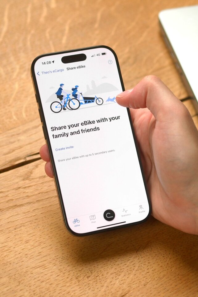 Een persoon zit aan tafel en heeft de eBike Flow-app op zijn smartphone geopend om zijn eBike met iemand te delen.