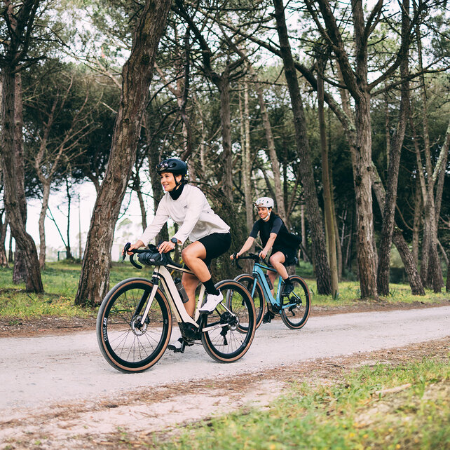 Twee eBike-rijders rijden op een weg, met bomen op de achtergrond.