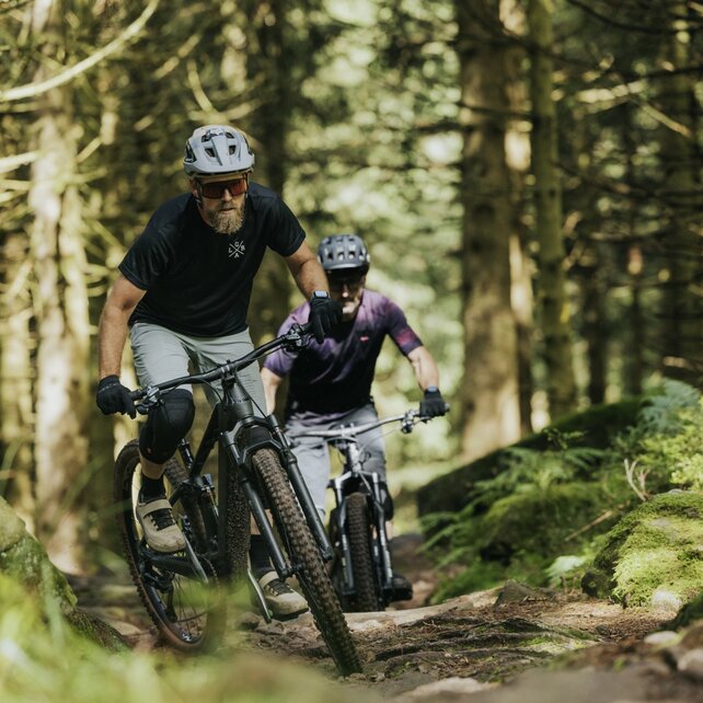 Un'area boschiva con due eMountain biker che pedalano uno dietro l'altro su un sentiero.