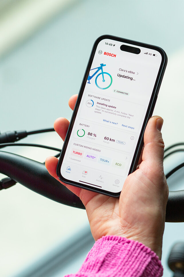 Eine Person hält ein Smartphone in der Nähe ihres eBikes und installiert Updates auf der Smartphone App.