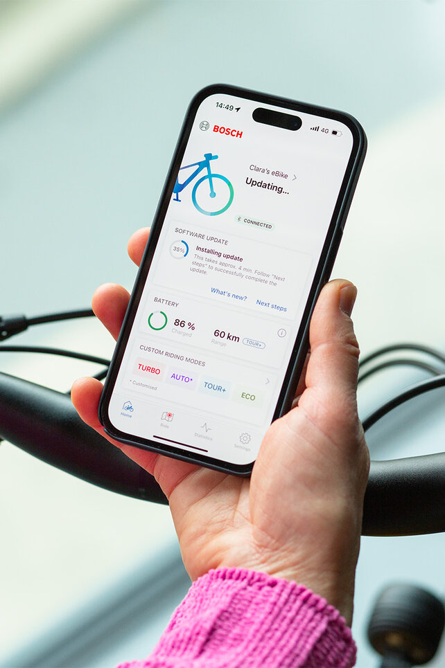 A person holds a smartphone near their eBike and installs updates using the smartphone app.