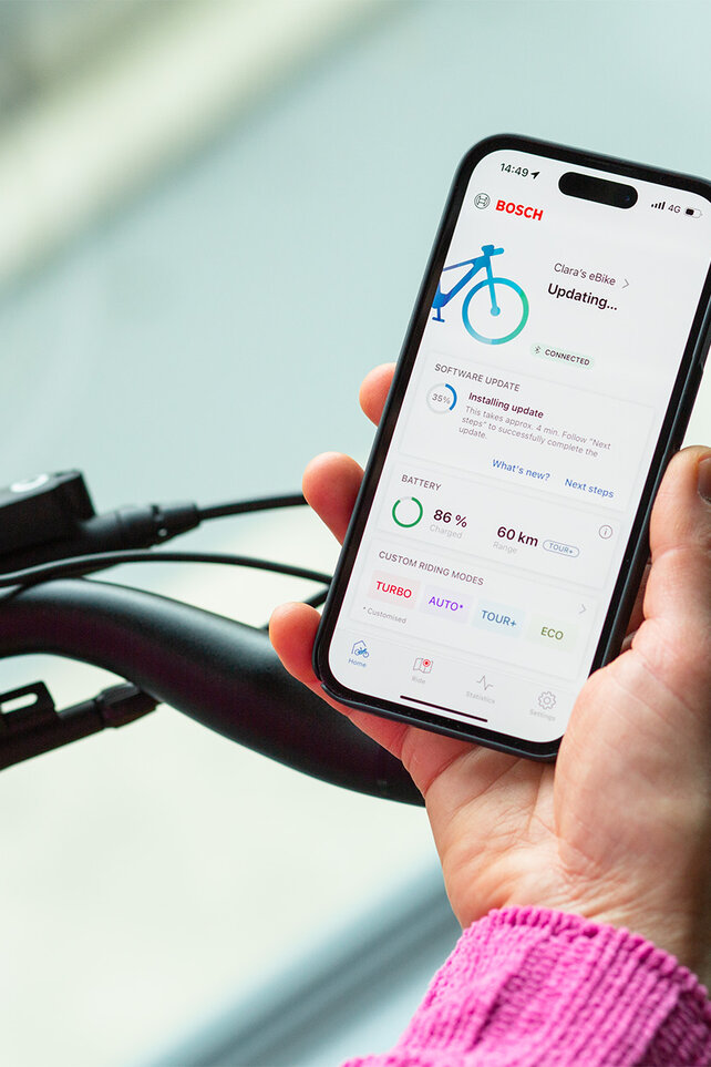 Une personne tient un smartphone près de son eBike et installe les mises à jour sur l’application pour smartphone.